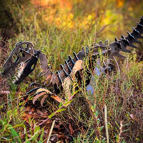 Velociraptor Dinosaur Sculpture Small Metal in Bush Setting Close Up